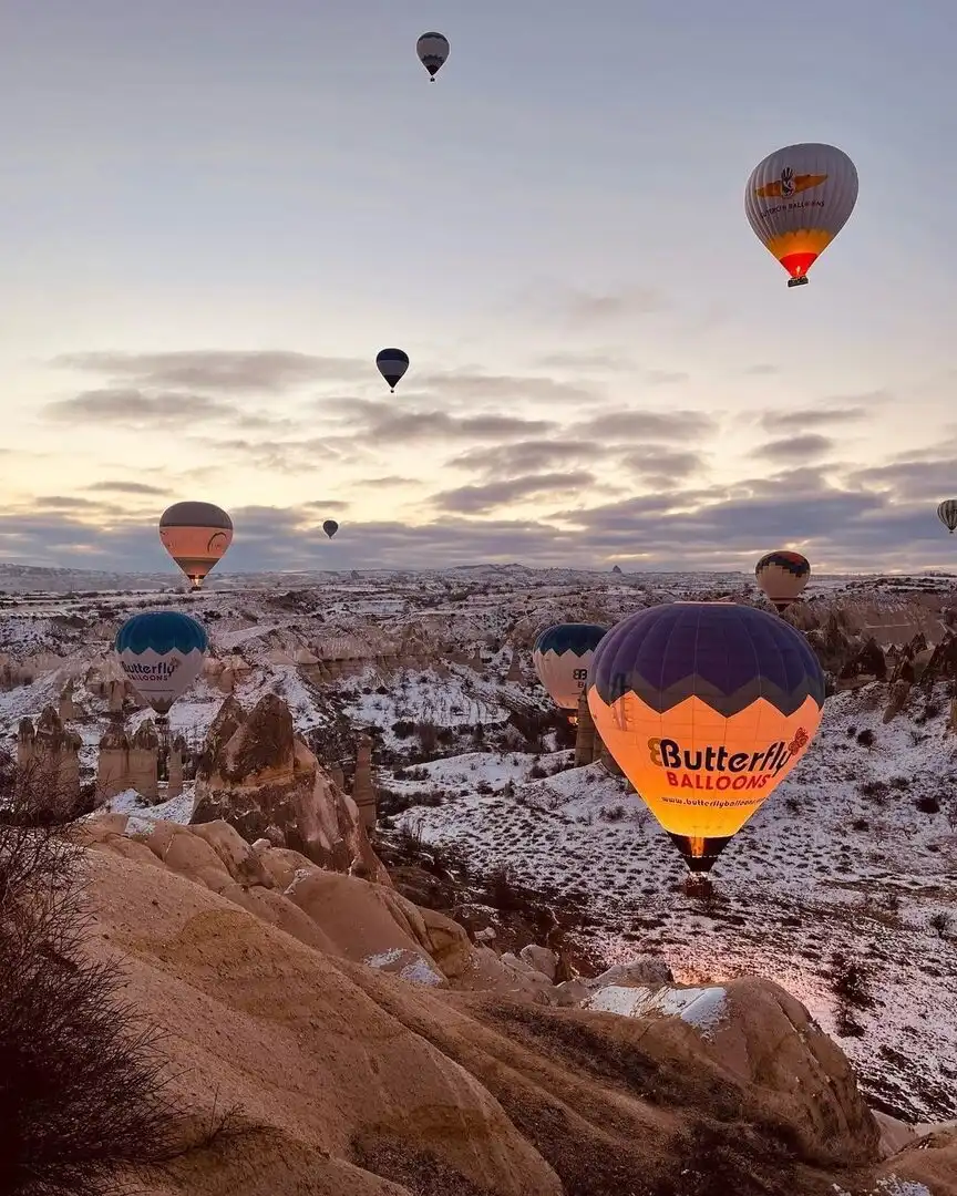 Воздушные шары над заснеженной Каппадокией на рассвете, зимний полёт в Гёреме, Турция