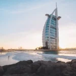Отель Burj Al Arab в Дубае на закате, волны и скалы на переднем плане — отдых в ОАЭ зимой