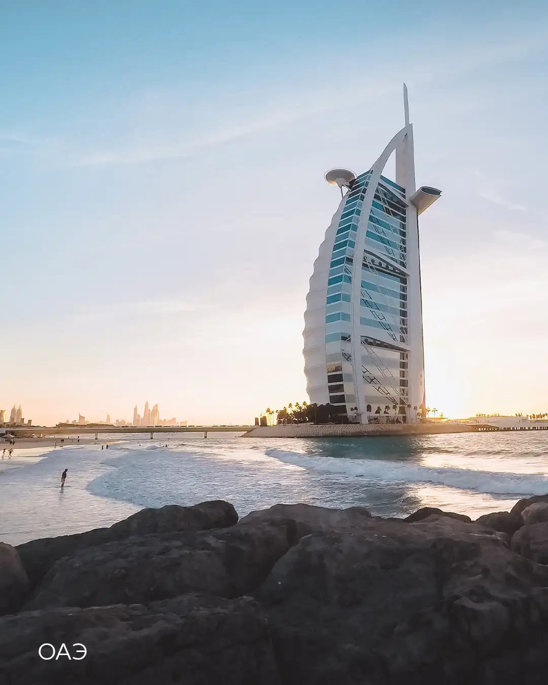 Отель Burj Al Arab в Дубае на закате, волны и скалы на переднем плане — отдых в ОАЭ зимой